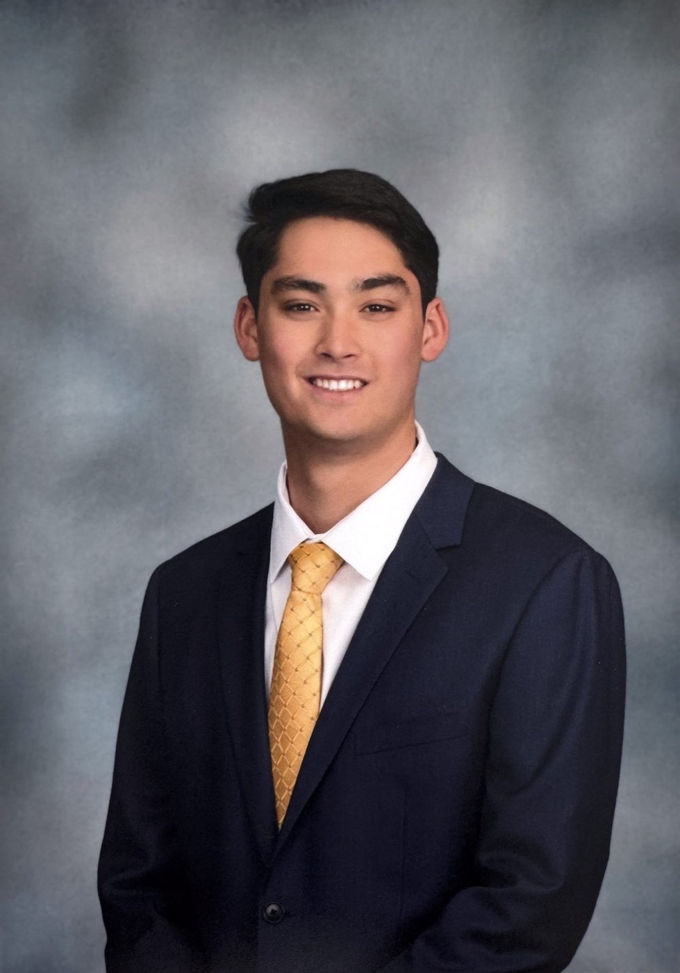 Portrait of Kevin Backer in a navy suit and gold tie